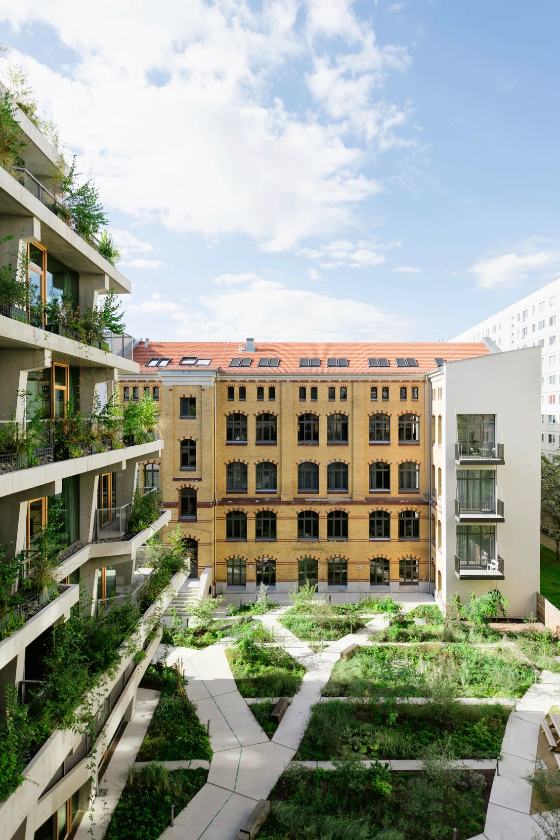 Nachhaltige Architektur: Modernes, begrüntes Bürogebäude mit großzügigem Innenhof neben einer historischen Backsteinfassade. Neu- und Altbau bieten einen architektonischen Kontrast.