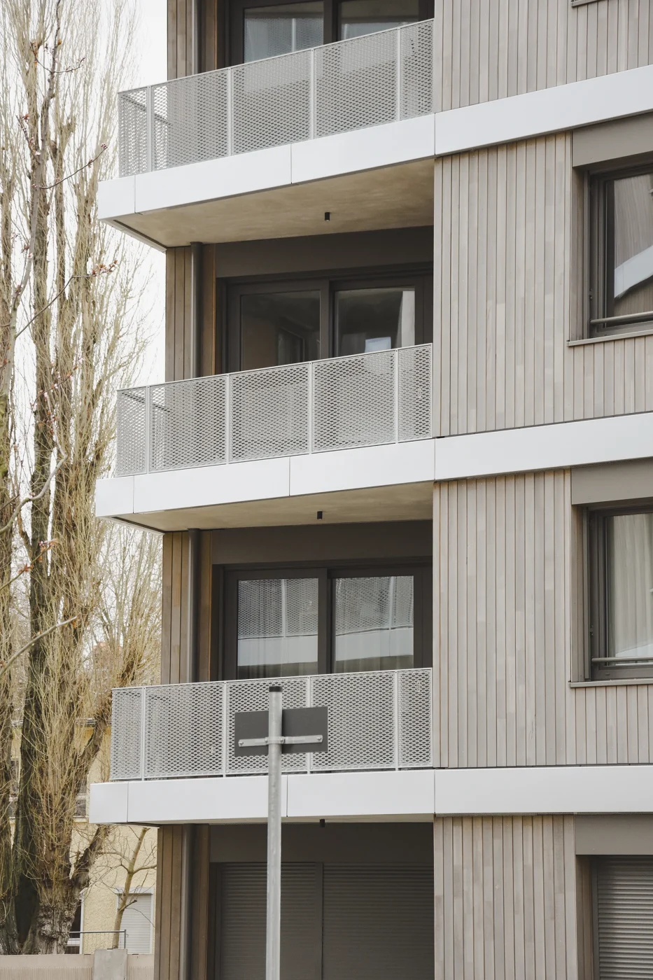 Fassadendetail des Wohnwerks mit vertikaler Holzschalung, auskragenden Balkonplatten und Brüstungen aus Streckmetall – Holzfassade im mehrgeschossigen Wohnungsbau.