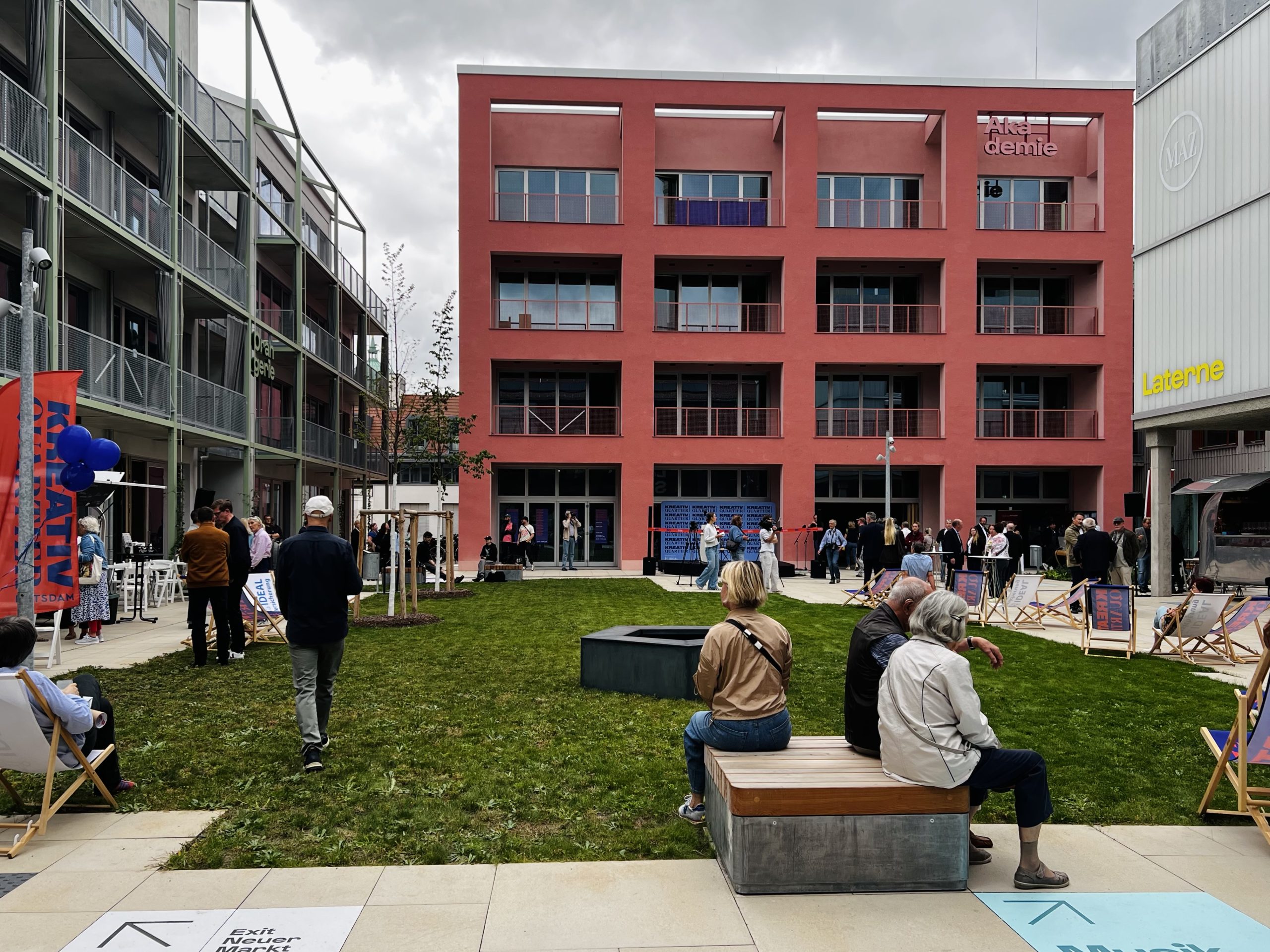 Blick auf die Akademie im Kreativ Quartier Potsdam während der Eröffnungsfeier, mit Gästen auf der Wiese und dem angrenzenden Gebäude „Laterne